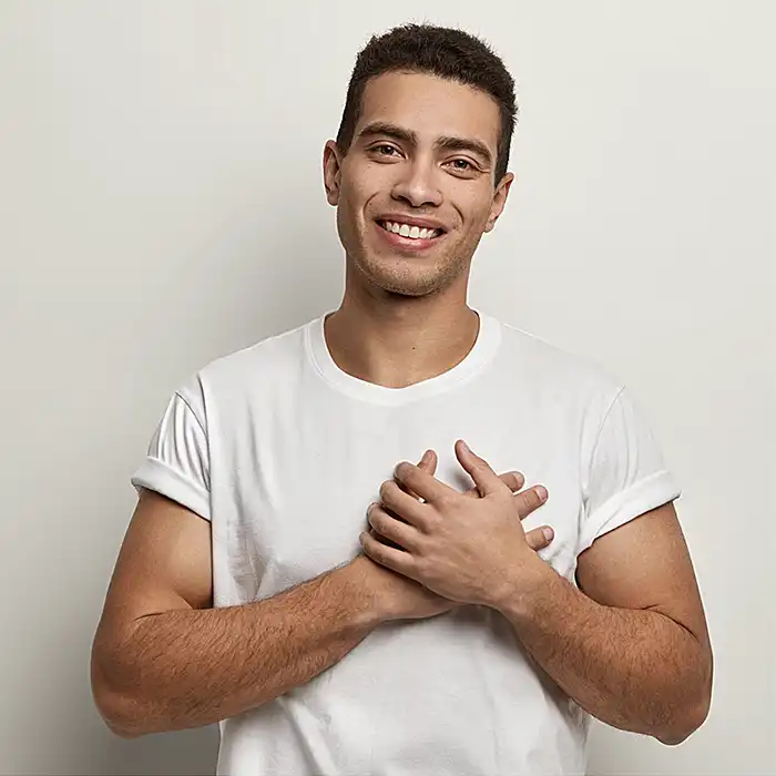 Retrato de una persona sonriente con camiseta blanca y las manos juntas sobre fondo claro