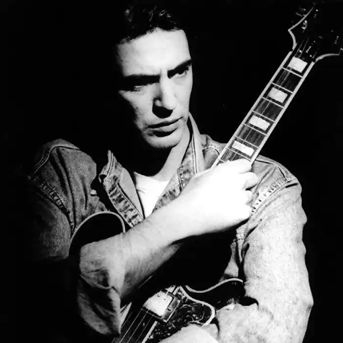 Fotografía en blanco y negro de una persona que sostiene una guitarra eléctrica sobre fondo oscuro