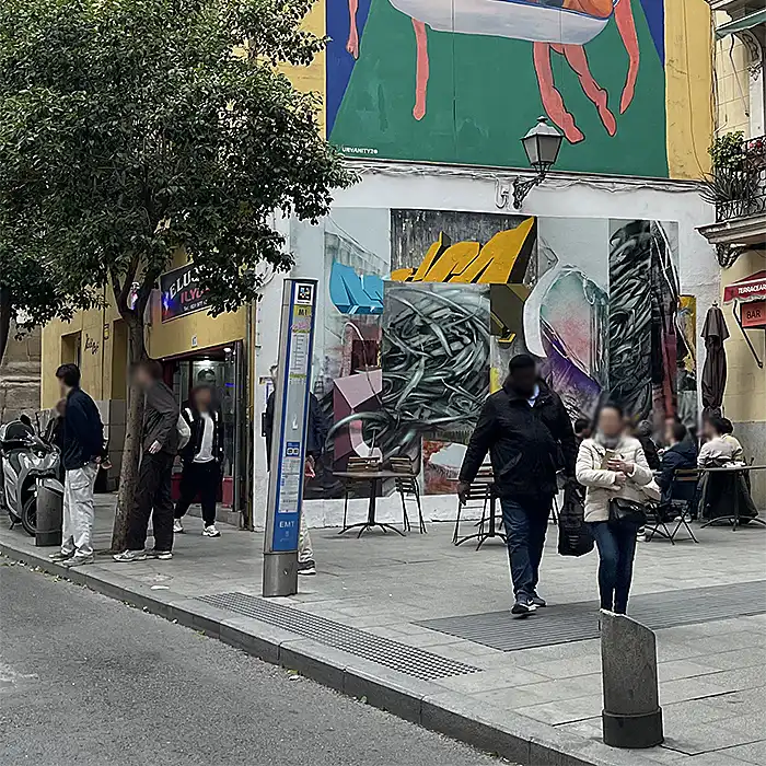 Calle con terraza, árboles y un mural en una fachada